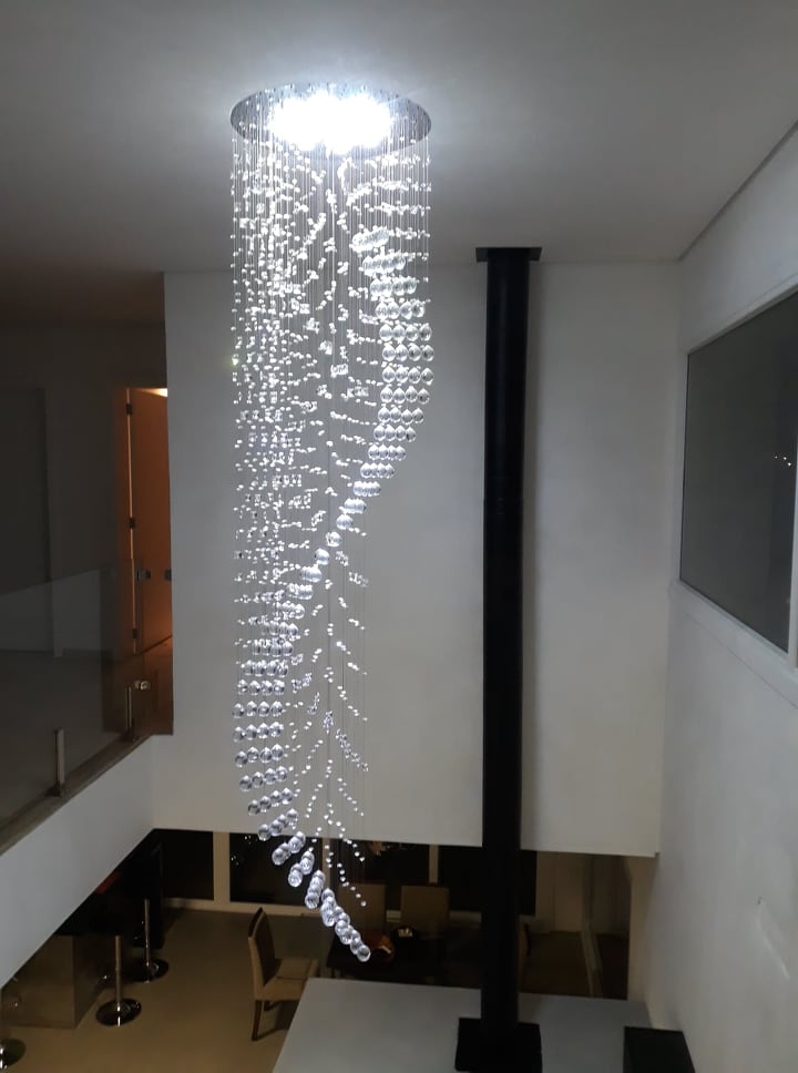 Lustre de cristal design S Rico instalado em sala com pé direito duplo, destacando cristais K9 legítimos da Linha Kria, ideal para ambientes sofisticados.